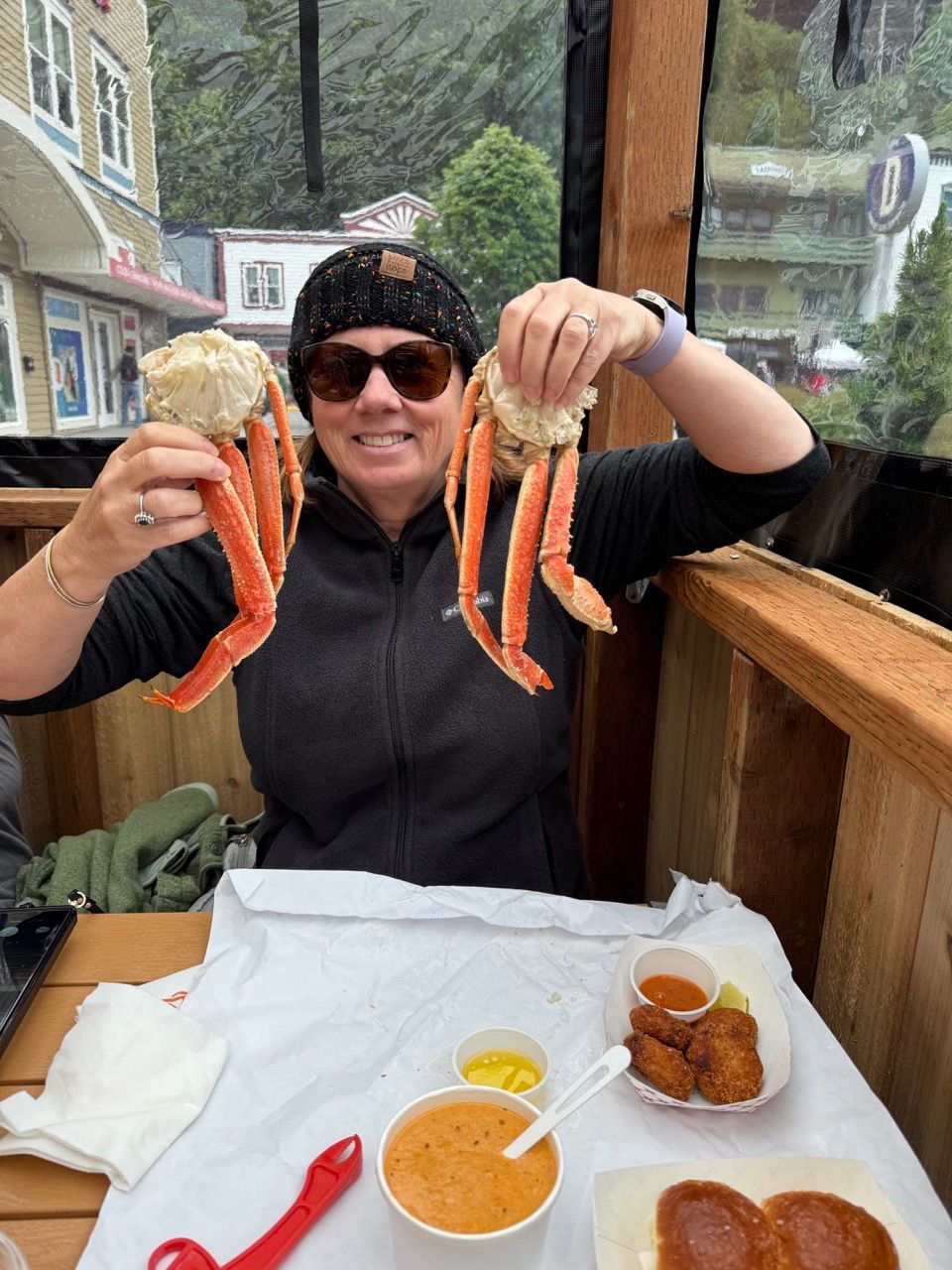 Person in sunglasses holds up two crab legs at a seafood restaurant table in Alaska