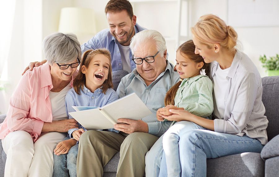 Family sitting on a couch, looking at a photo album. Two young girls laughing.