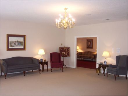 A beige-walled room with a chandelier, couches, and an open doorway leading to another room.