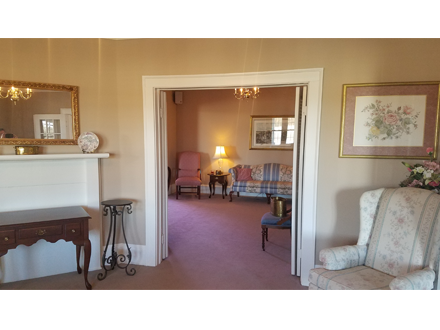 Interior with open doorway, showing a room with pink carpet, furniture, and a chandelier.
