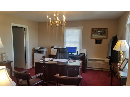 An office with a desk, chairs, printer, and chandelier on a red carpet.