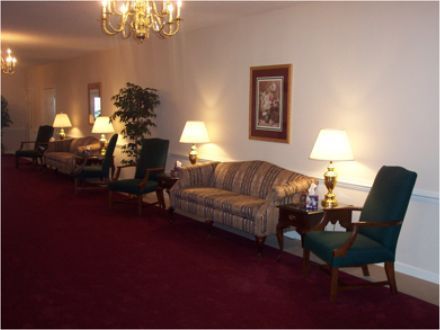 A hallway with sofas, chairs, lamps, and a red carpet. The walls are light-colored.