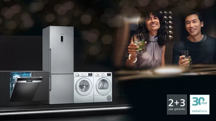 Een man en een vrouw staan naast een koelkast, wasmachine en droger.