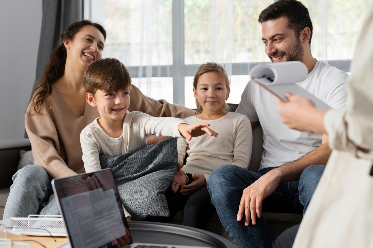 A family is sitting on a couch in front of a laptop computer.