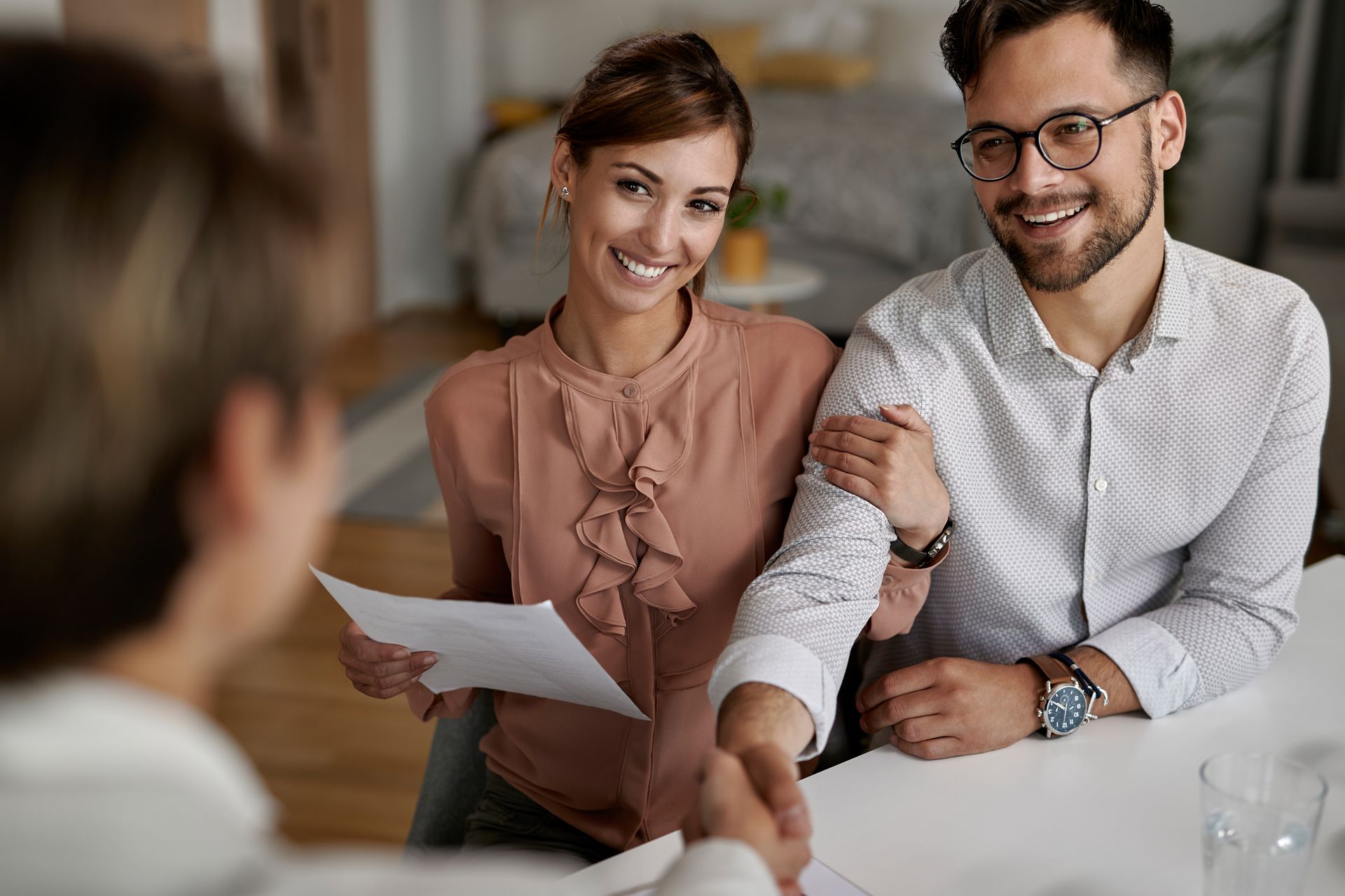 A man and woman are shaking hands while sitting at a table. 