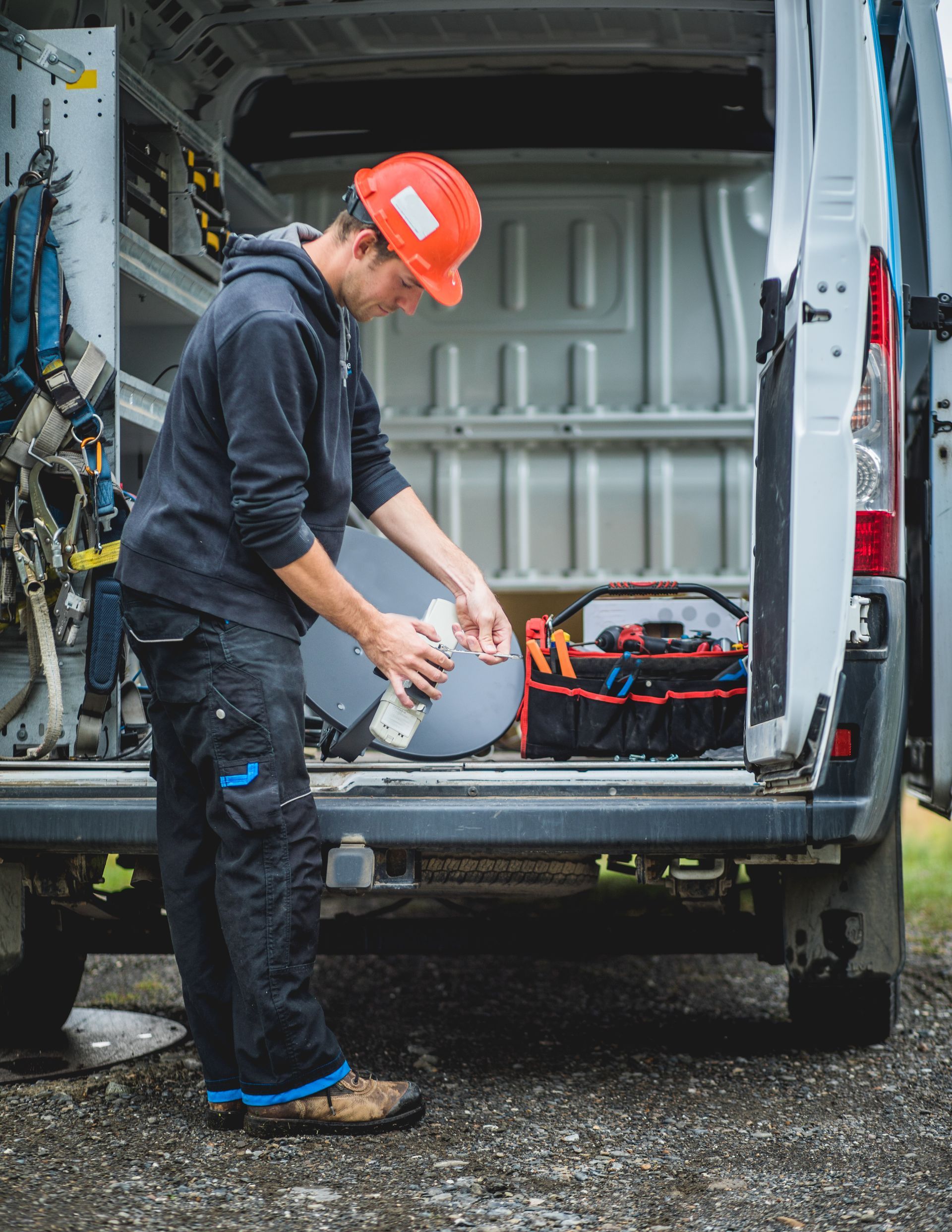 A man is working on a satellite dish in the back of a van.