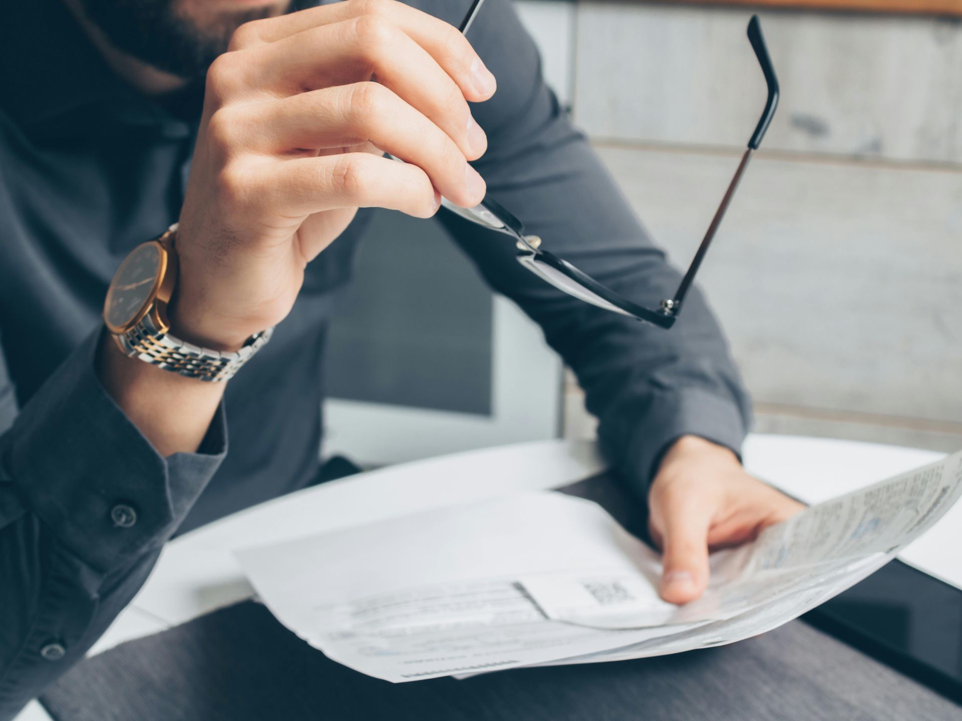 A man wearing glasses is holding a pen and looking at a piece of paper.