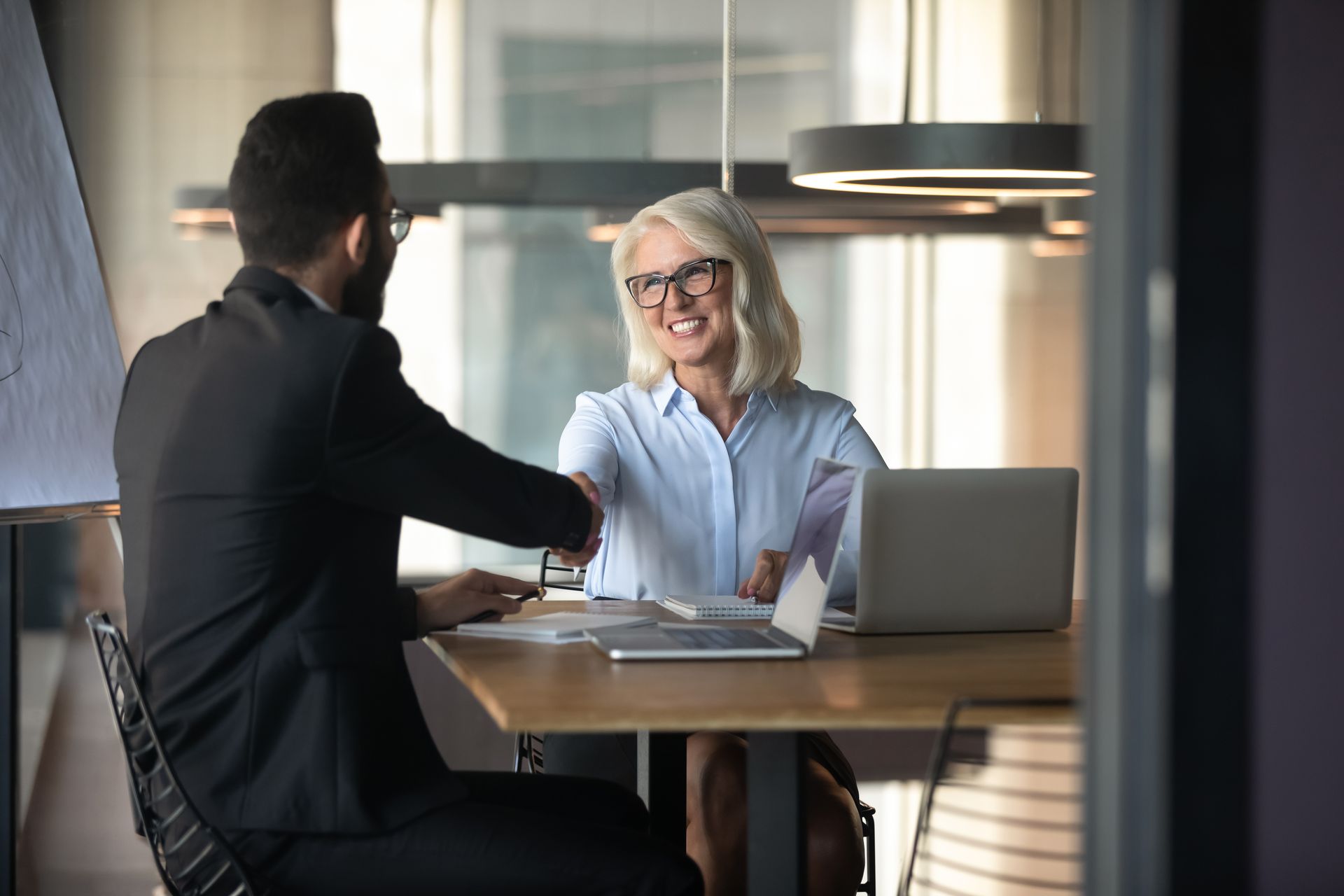 A man and a woman are shaking hands at a table. 