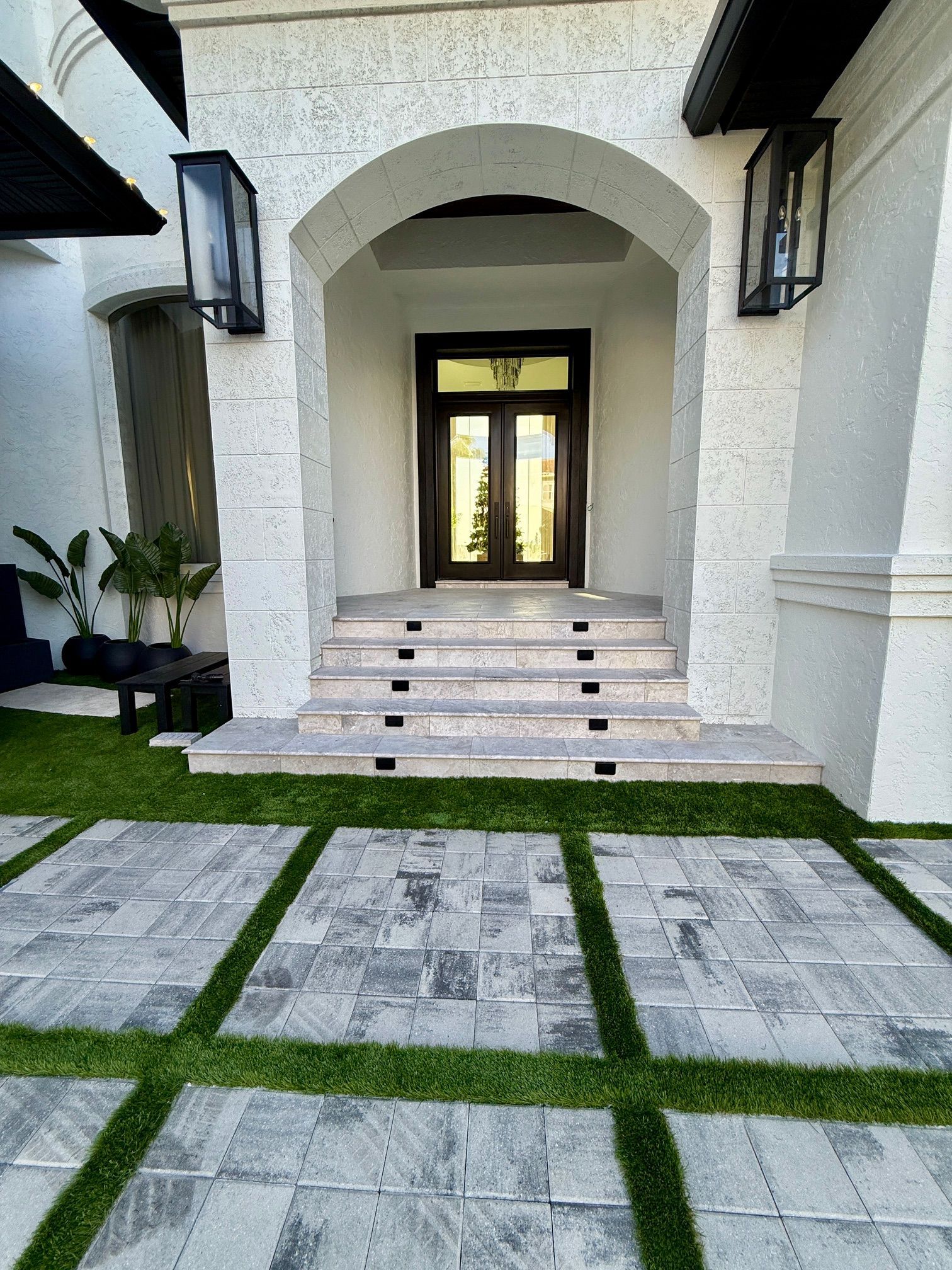 Turf inlay between paver squares utilizing Flagstone Commonwealth pavers in White Pewter leading to a custom marble staircase with lighting