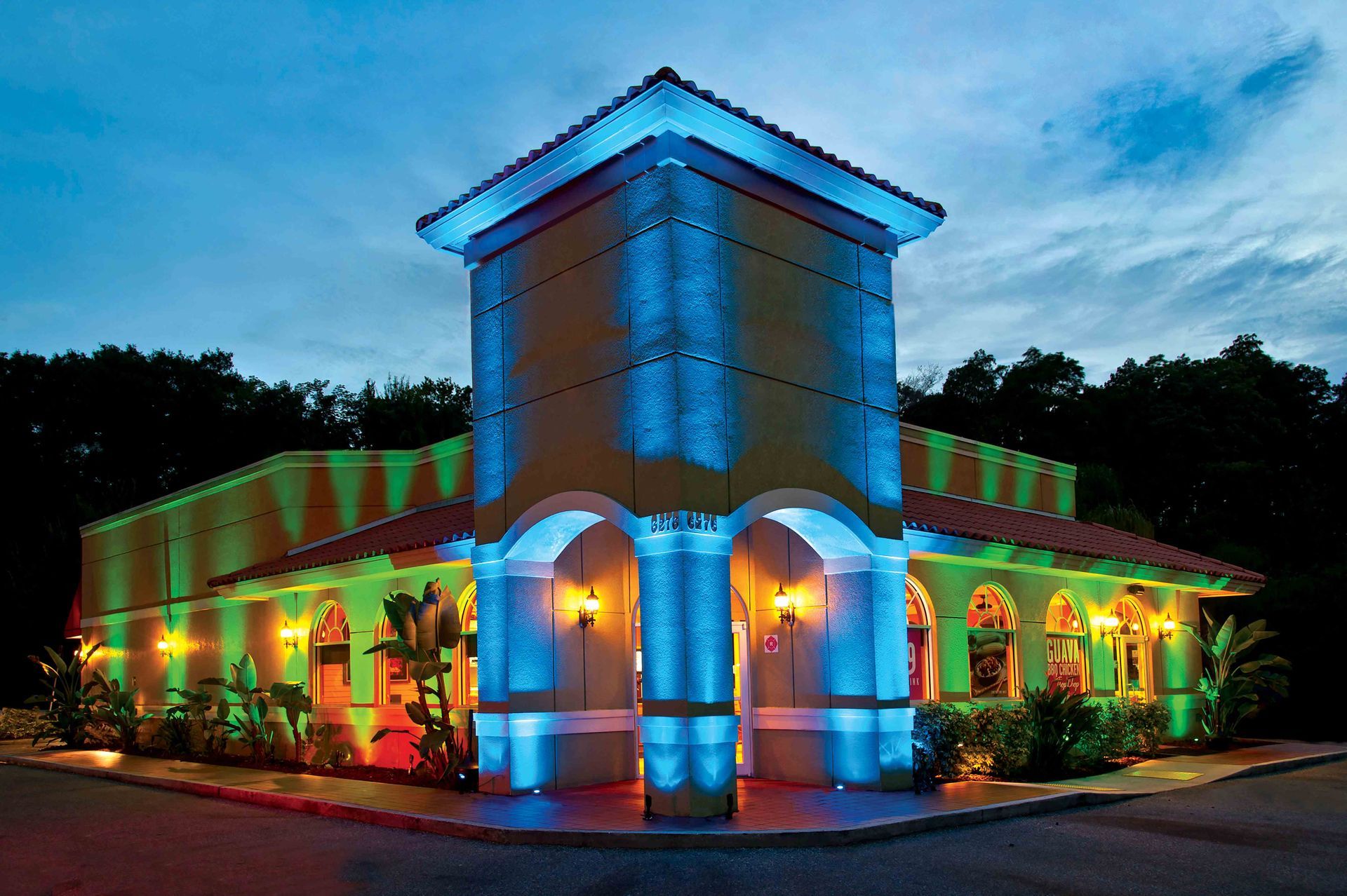 Restaurant with tan walls, blue and green lighting, and arched windows at dusk.