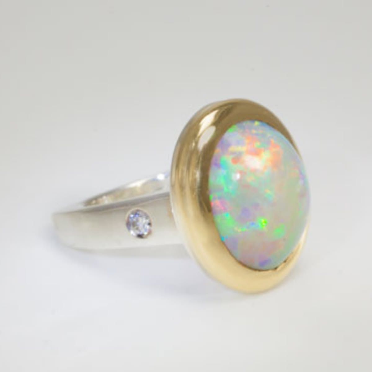 Silver ring with oval opal and gold bezel on a white background