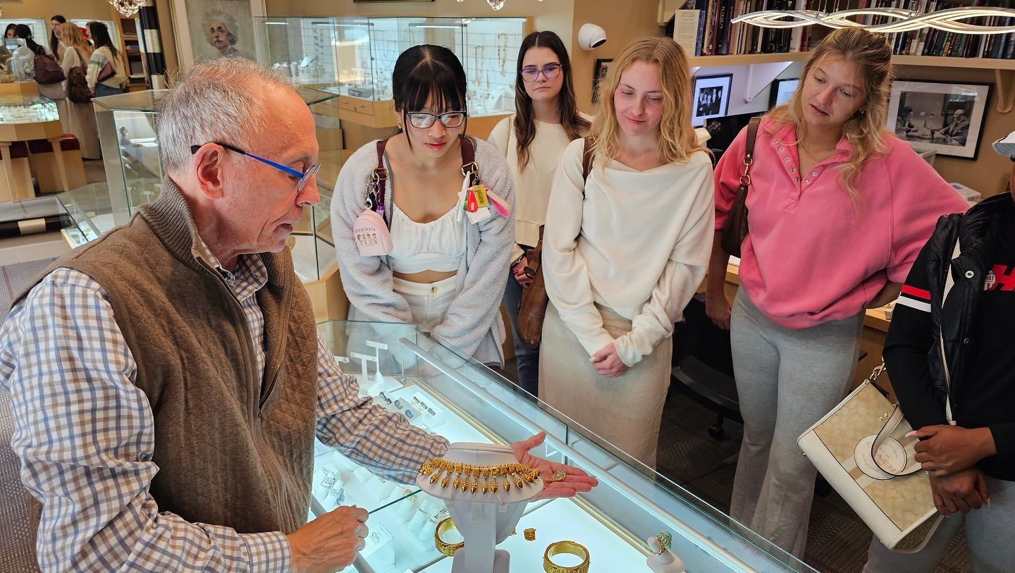 Museum guide showing artifacts in a glass display case to a small group in a room with framed photos.