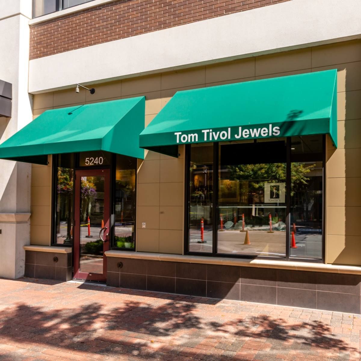 Storefront with green awnings labeled “Tom Tivol Jewels” on a sunny street.