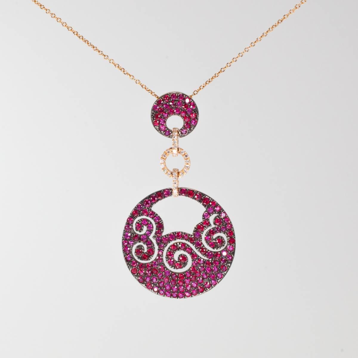 Pink jeweled pendant necklace with a circular filigree charm on a gold chain