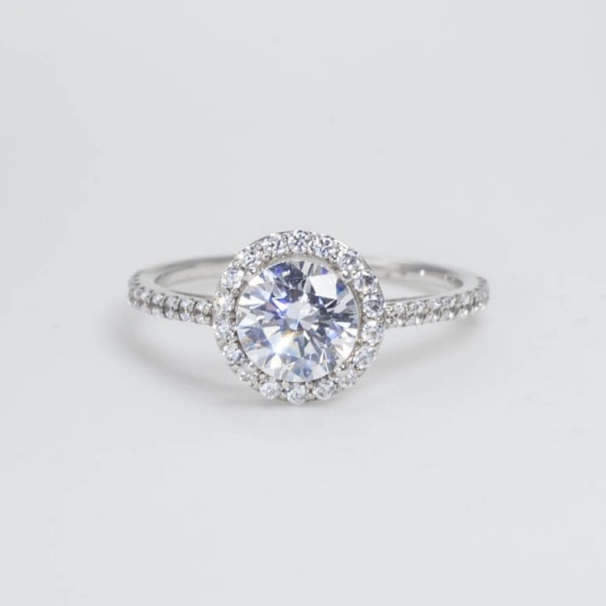 Silver ring with a round diamond halo and pavé band on a white background