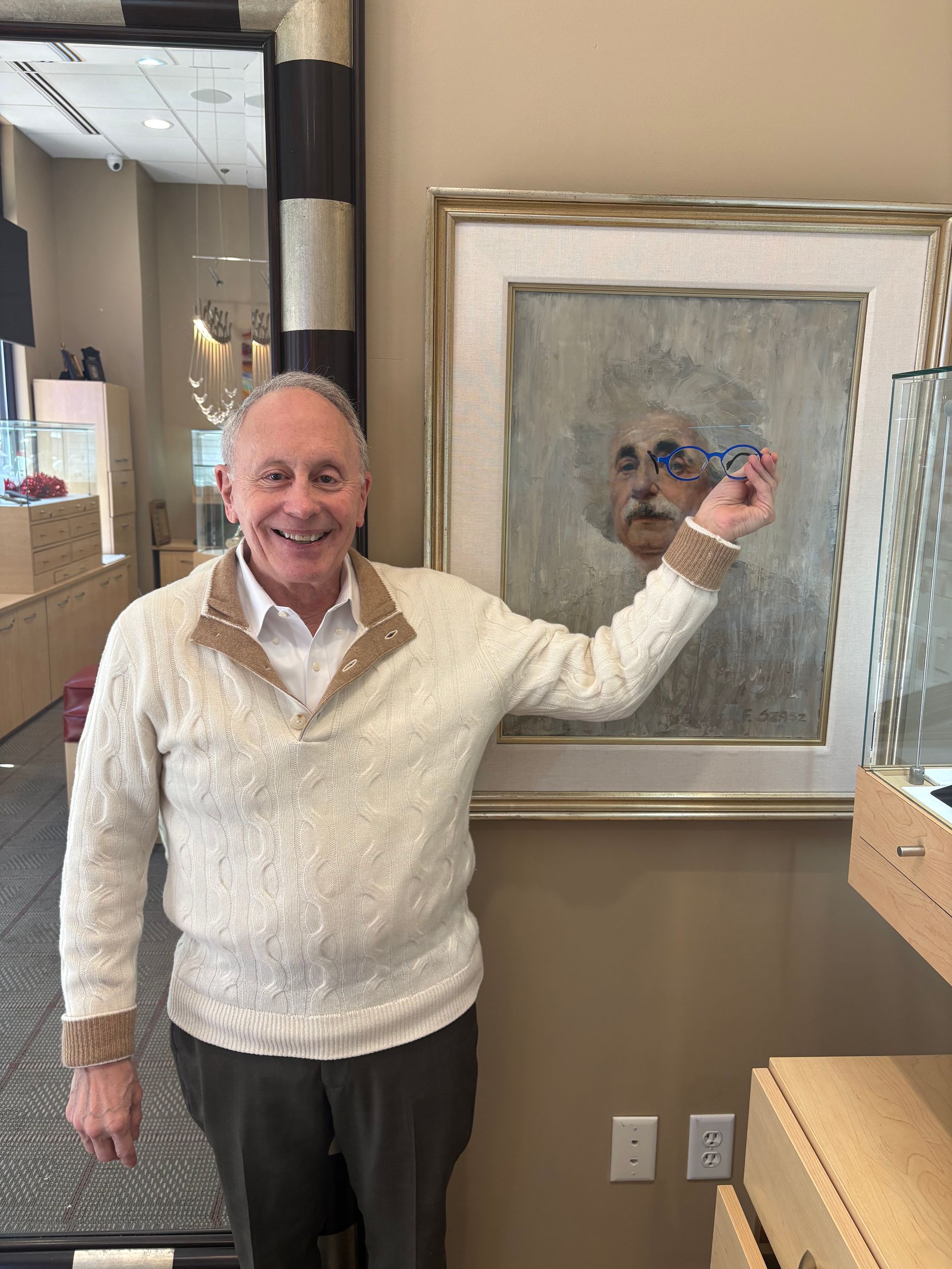 Smiling man in cream sweater points at framed portrait in a gallery or office setting
