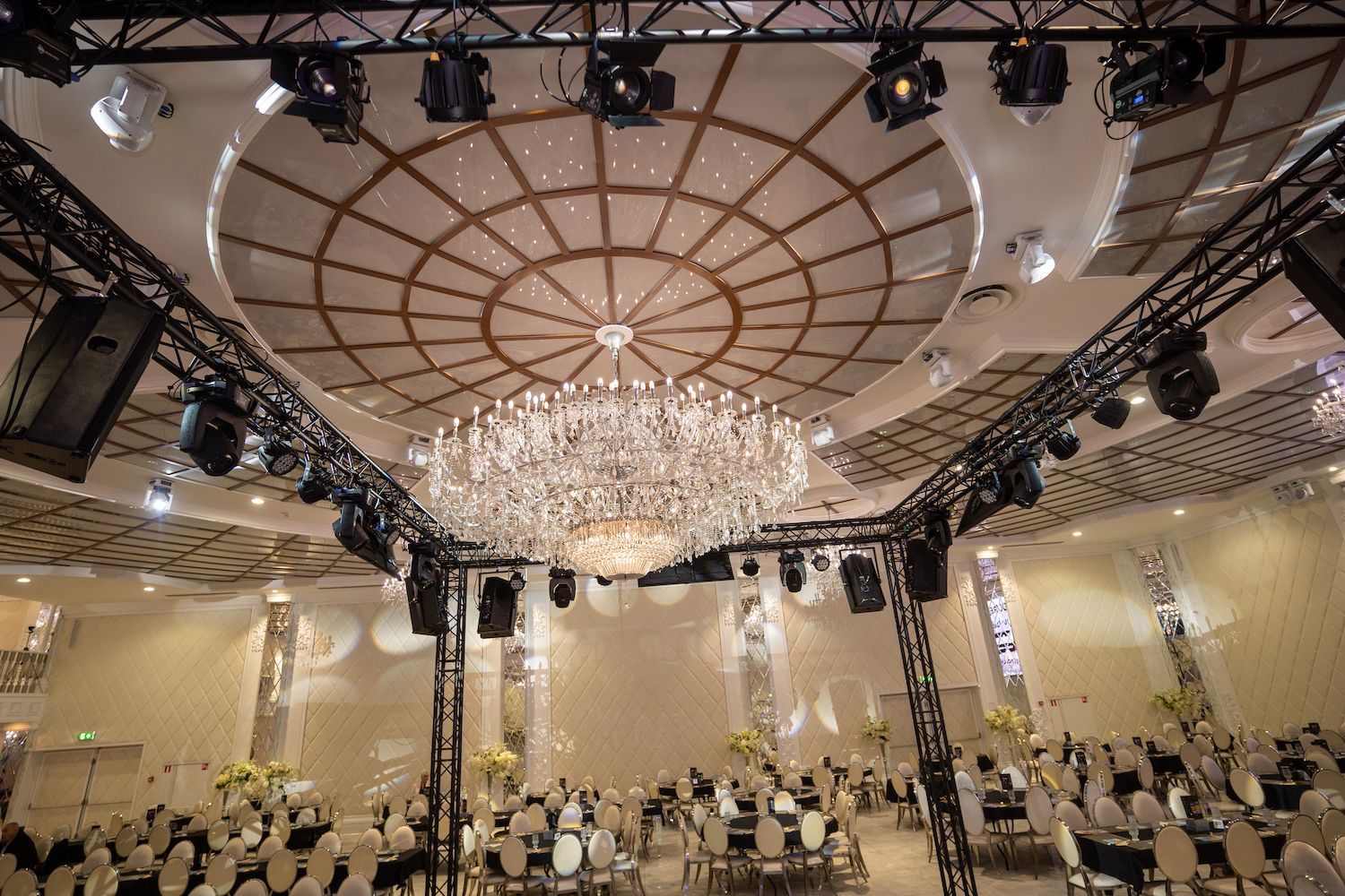 Elegante feestzaal met kroonluchters, een sierlijk plafond en ronde tafels, perfect voor een evenement.