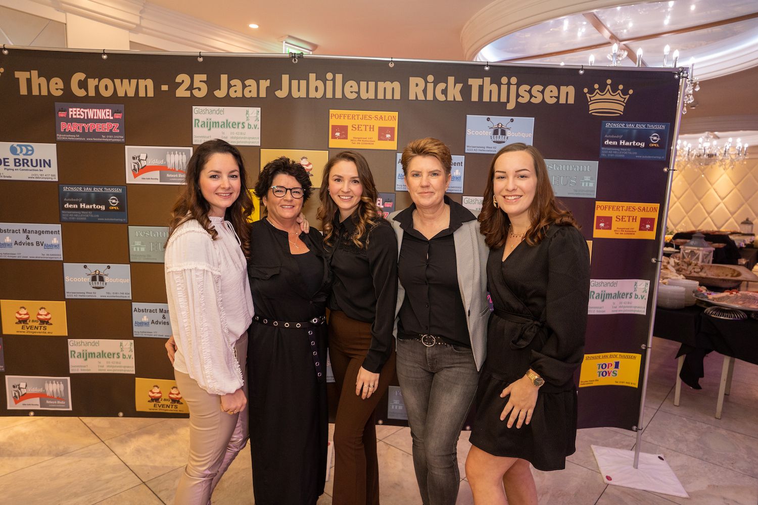 Vier mensen poseren voor een evenementenwand met de tekst 