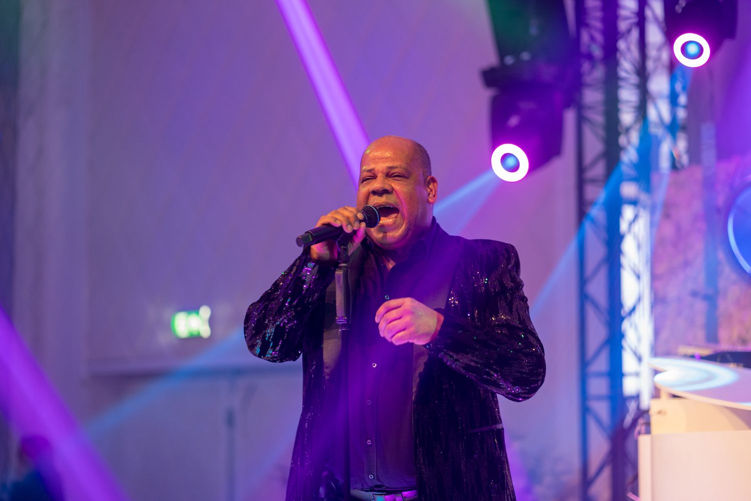 Zangeres treedt op een podium op onder paarse lichten, met een microfoon in haar hand, en zingt vol overgave.