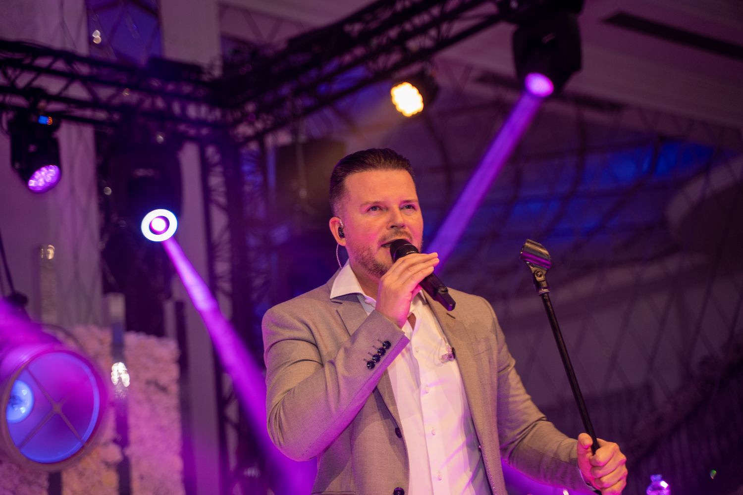 Zangeres treedt op een podium op onder paarse lichten, met een microfoon in haar hand, en zingt erin.