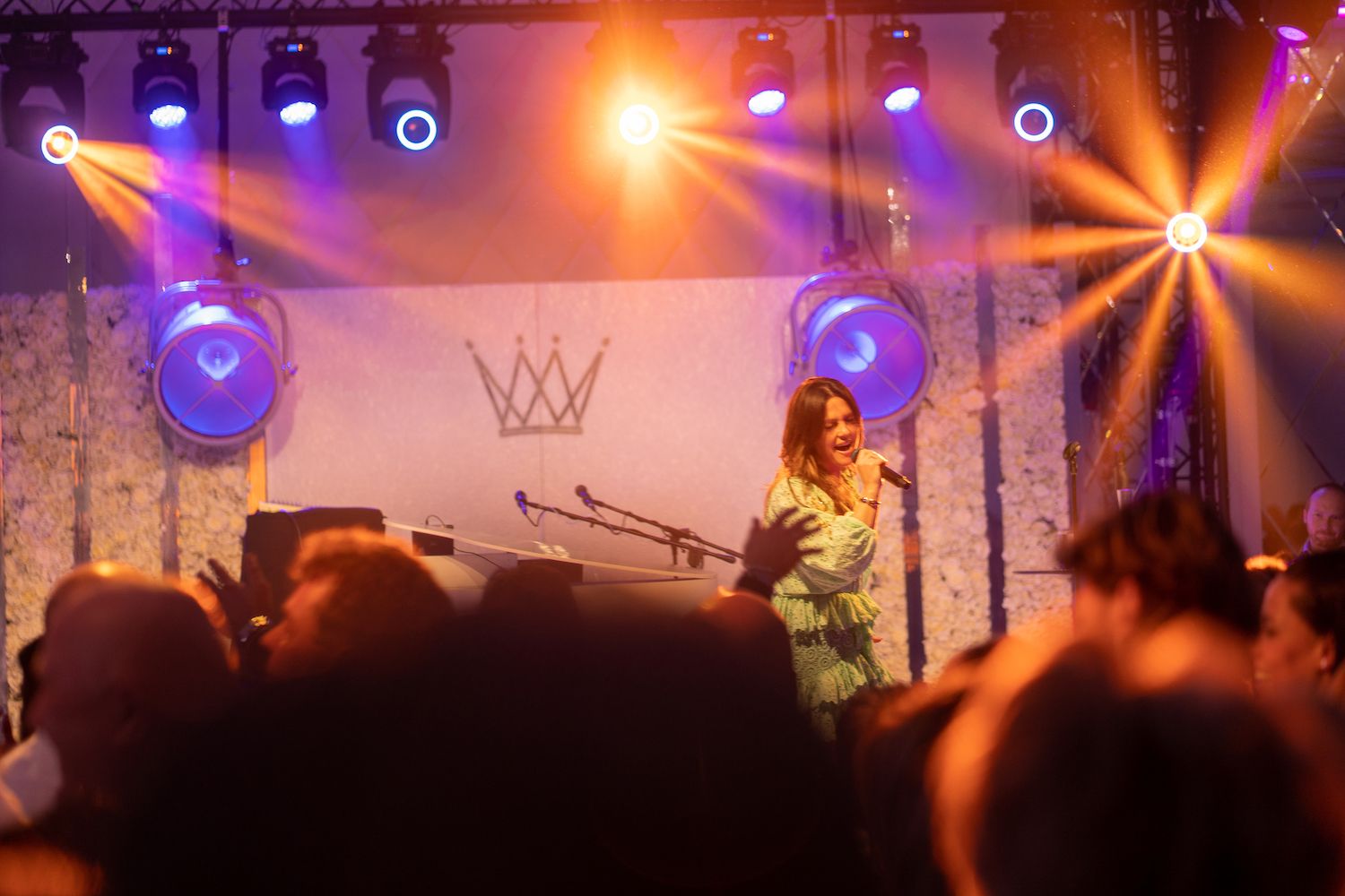 Zangeres op het podium onder paarse en oranje lichten, optredend voor een wazig publiek.