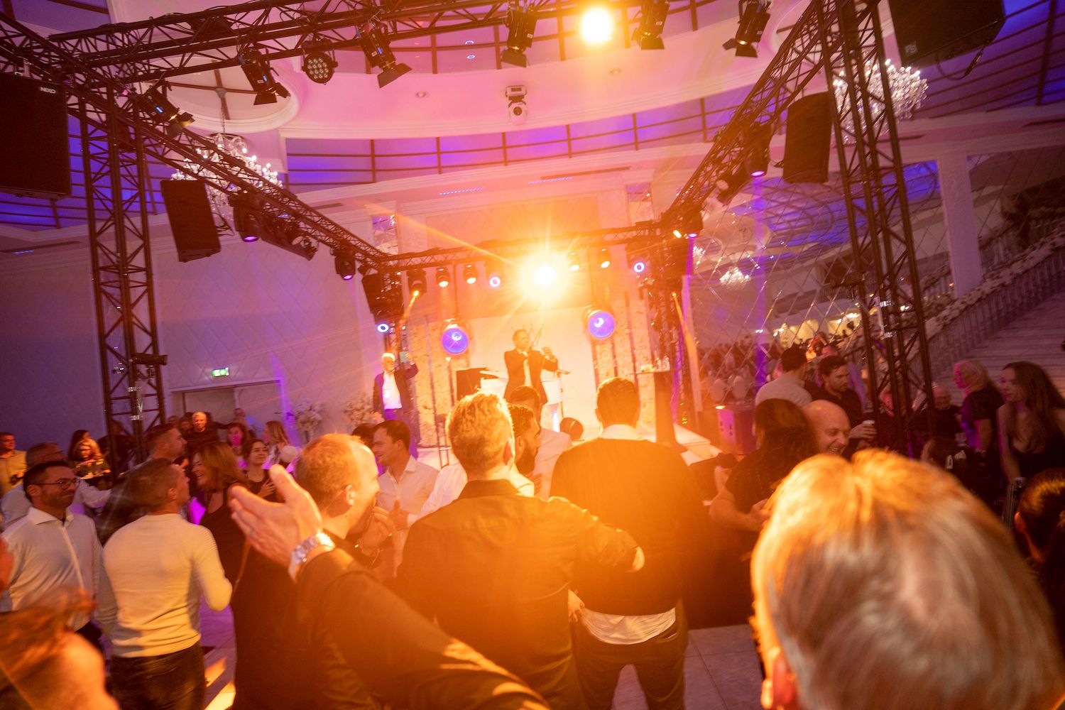 Een menigte danst op een binnenfeest onder feloranje podiumverlichting.