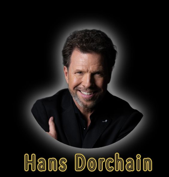 Portret van Hans Dorchain, lachend in een zwart shirt tegen een donkere achtergrond.