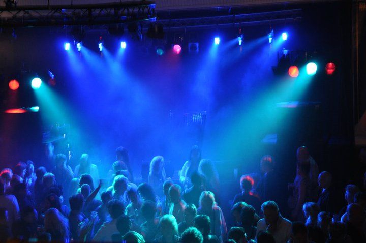 Blauwe en paarse podiumlichten schijnen boven een dansende menigte in een donkere concertzaal.