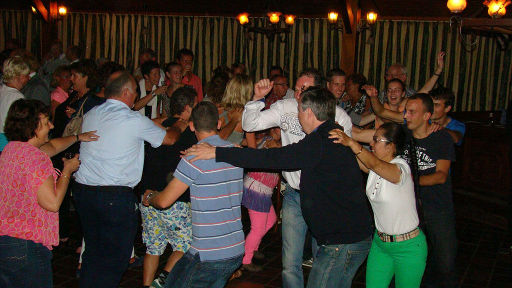 Mensen dansen in een volle club, met hun armen omhoog en warme oranje lichten op de achtergrond.