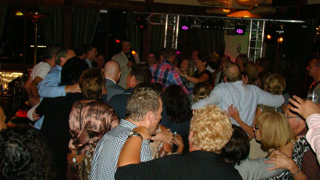 Een overvolle dansvloer in een nachtclub, waar mensen zich mengen onder gedimd licht en paarse accenten.