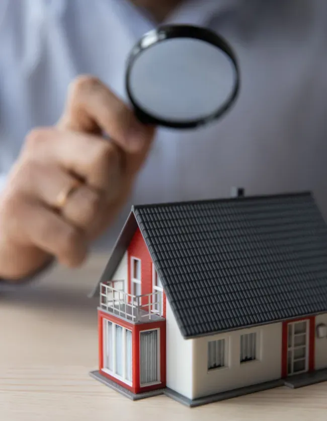 A man is looking at a model house through a magnifying glass.