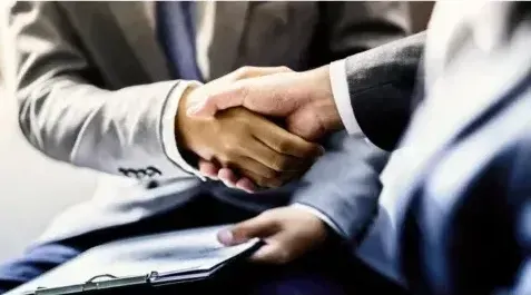 A man in a suit and tie is shaking hands with another man.