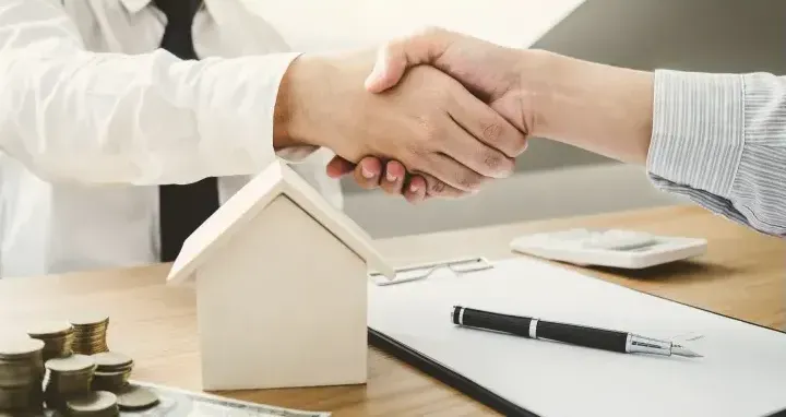A man is shaking hands with a woman in front of a model house.