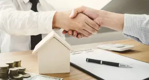 A man is shaking hands with a woman in front of a model house.