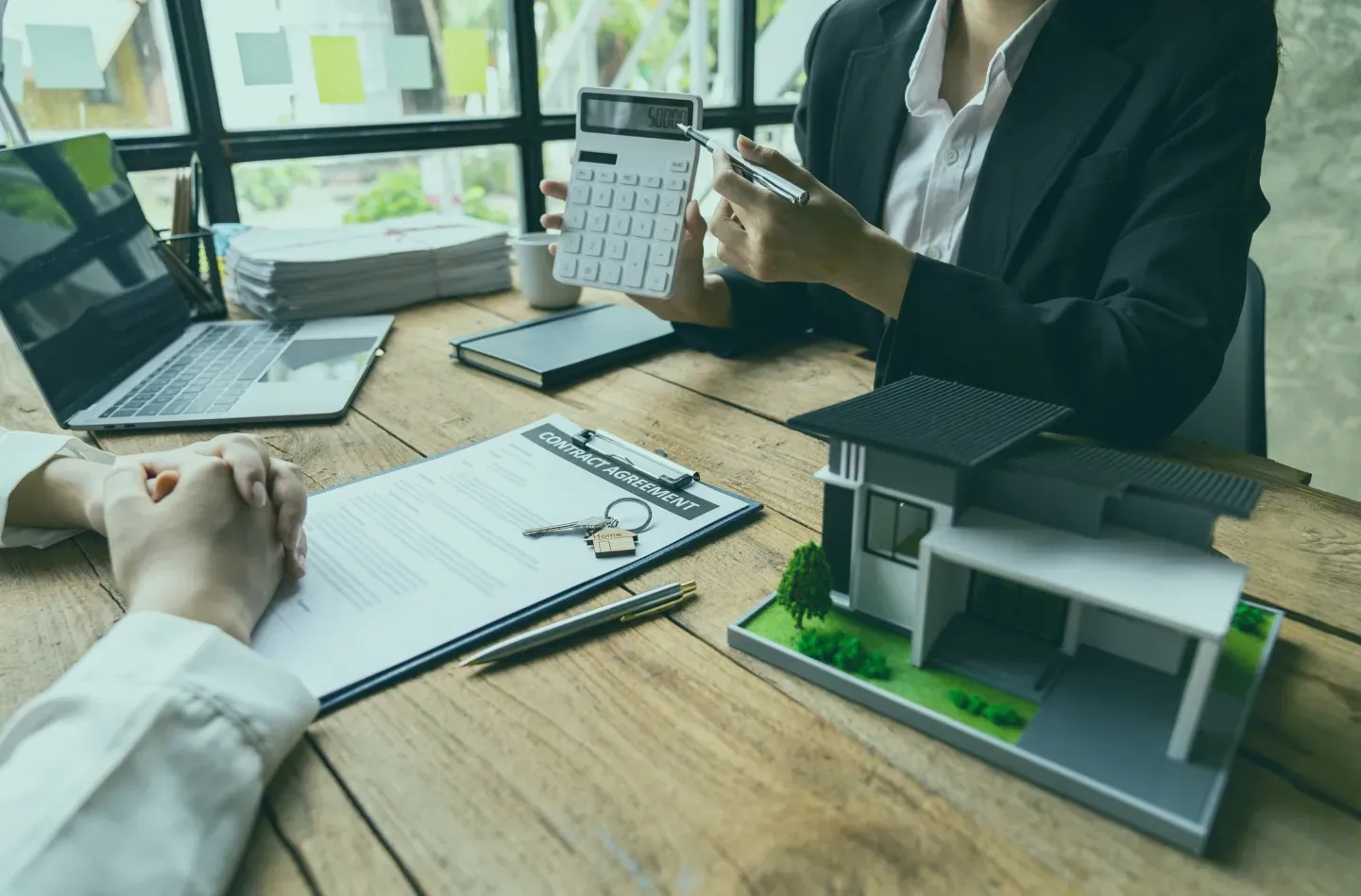 A woman is sitting at a table holding a calculator and a model house.