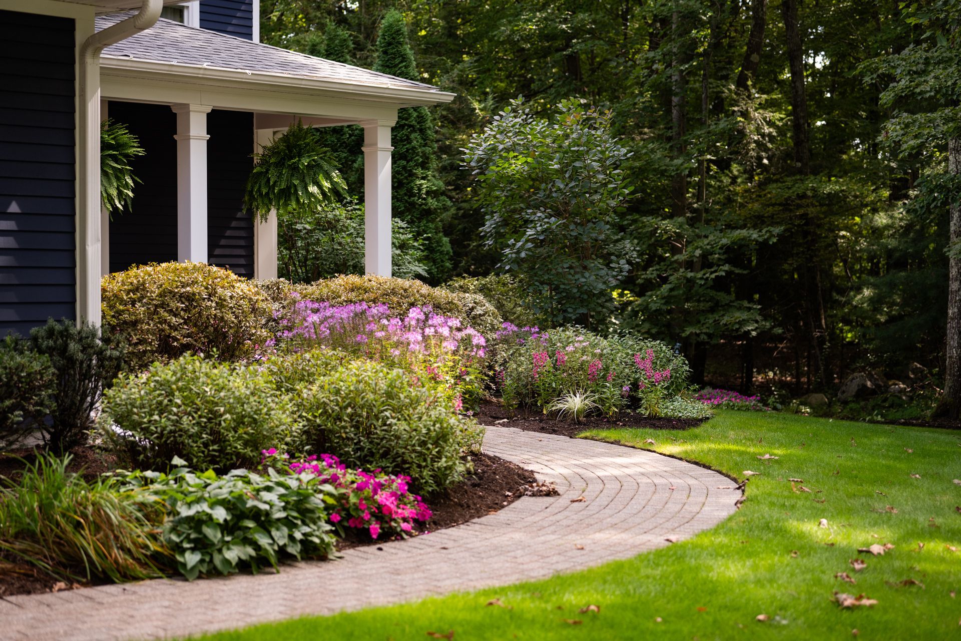 A house with a porch and a walkway leading to it surrounded by flowers and bushes.