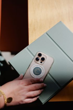 Hand holding a pink phone over two stacked pale green gift boxes on a wooden surface.