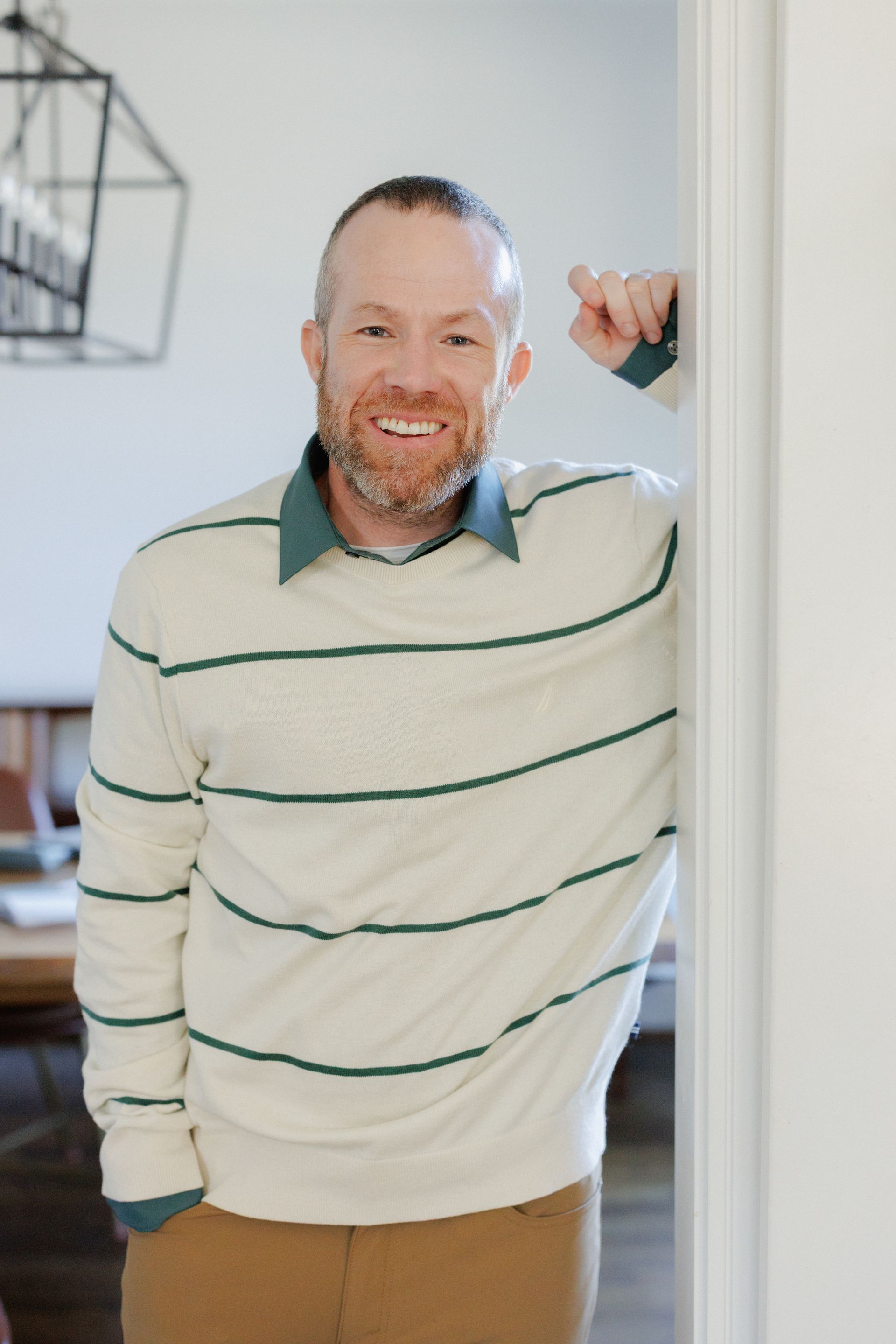 Smiling man in striped sweater leaning against a doorway in a bright room