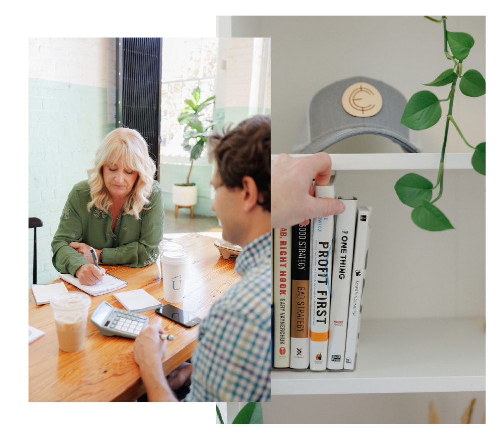 Two people discussing documents at a bright table beside a shelf with books and a trailing plant