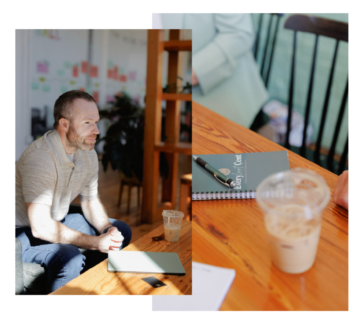 Man seated indoors at a wooden table beside an iced coffee and notebook, looking off to the side.