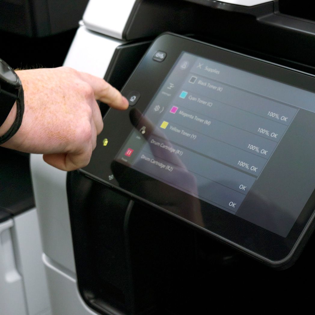 Person's finger pressing a button on a printer's touchscreen. Display shows ink levels.