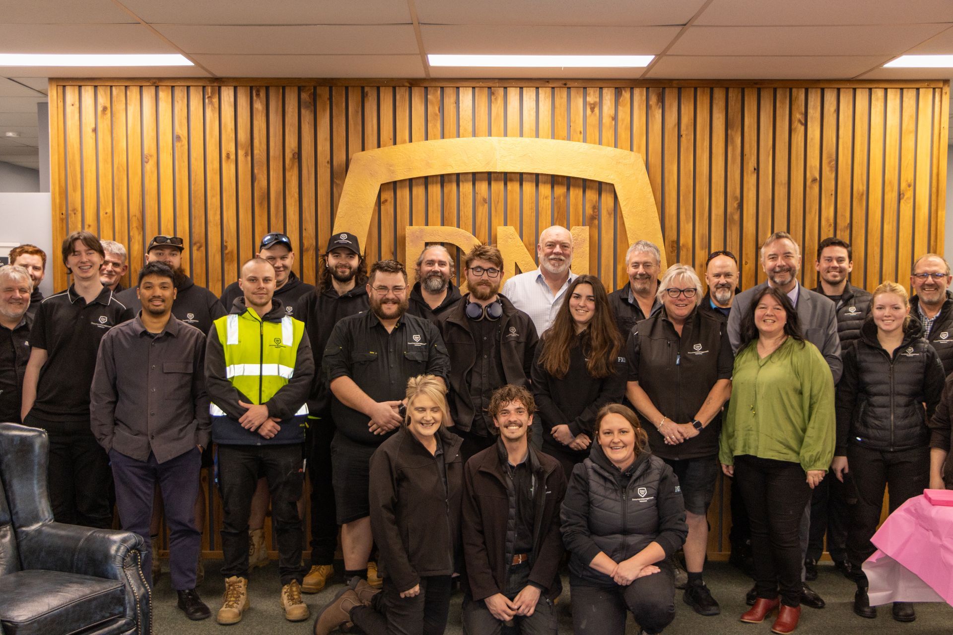 Group photo posing in front of Document Management Tasmania wood panel logo. Sonia's 25th Anniversary.