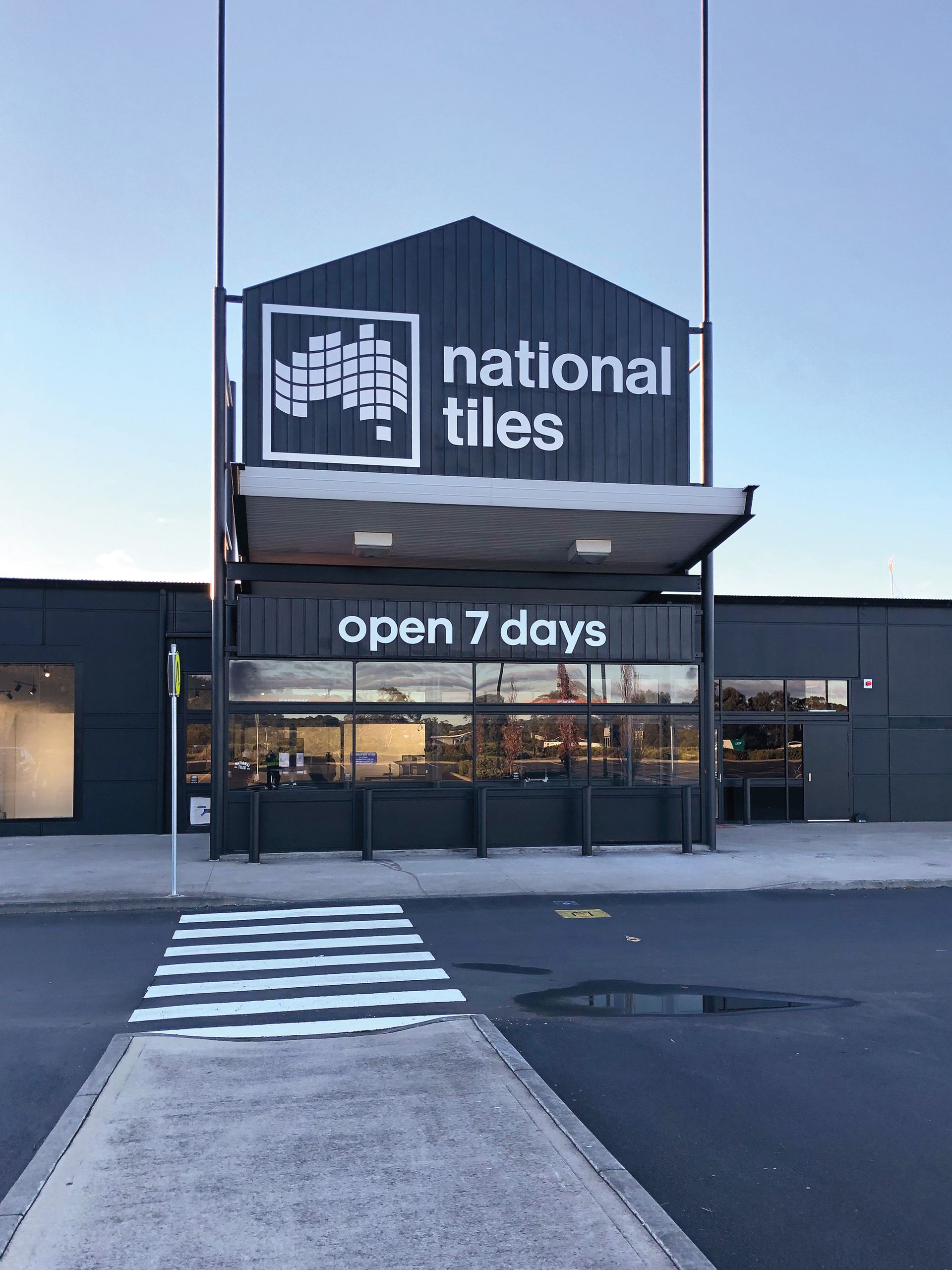 Exterior of a National Tiles store with the sign “open 7 days”. A crosswalk leads to the entrance.