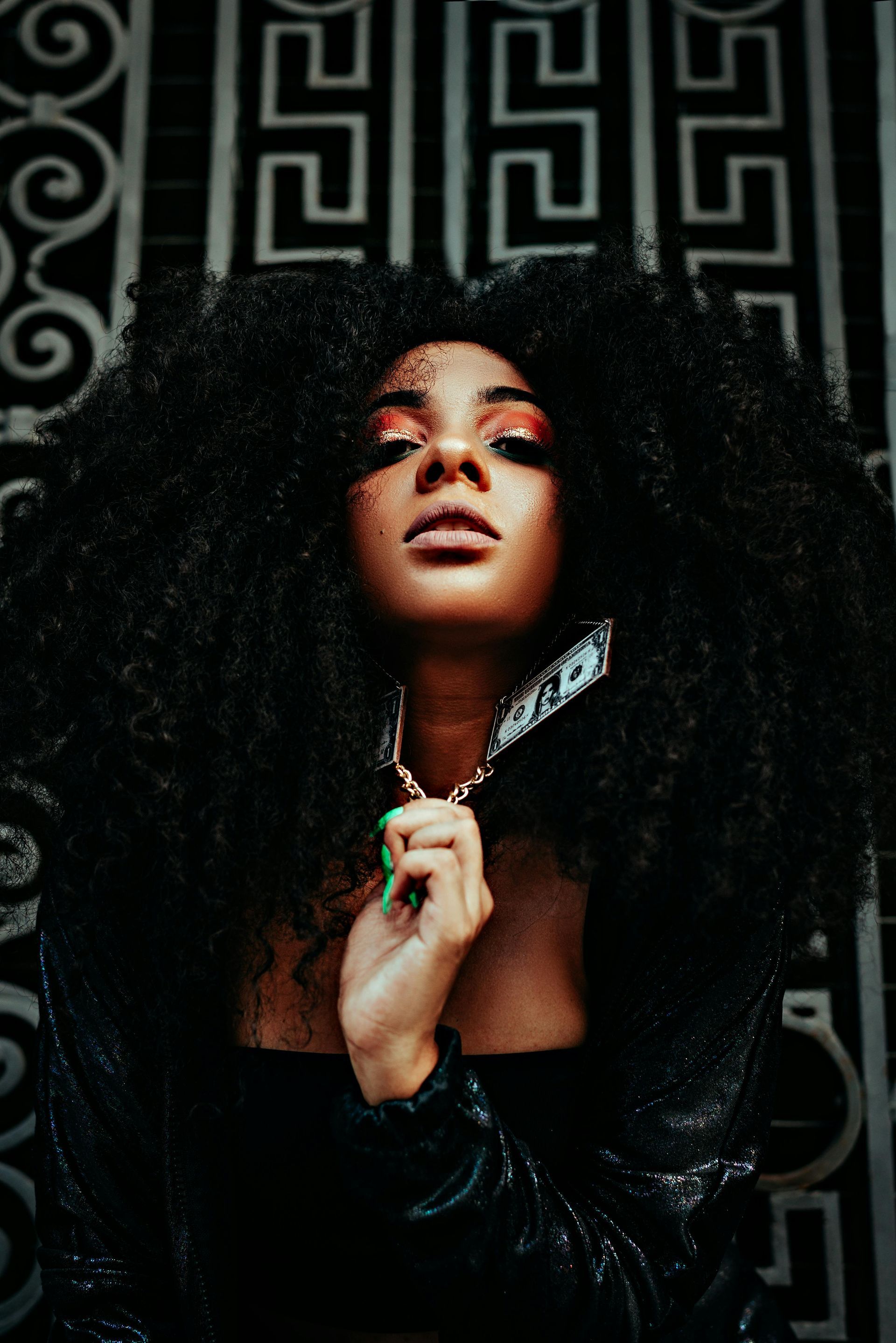Woman with large afro, holding object, front of black and white ornate backdrop.
