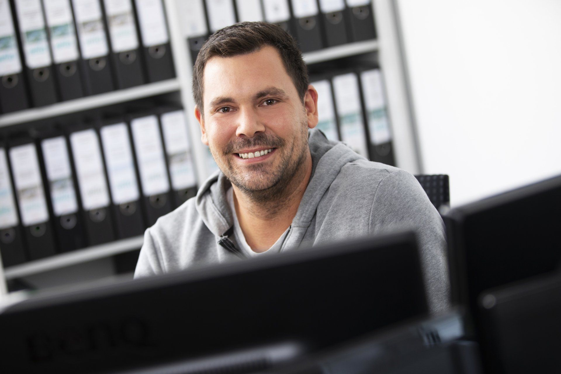 Ein Mann lächelt, während er vor einem Computermonitor sitzt.
