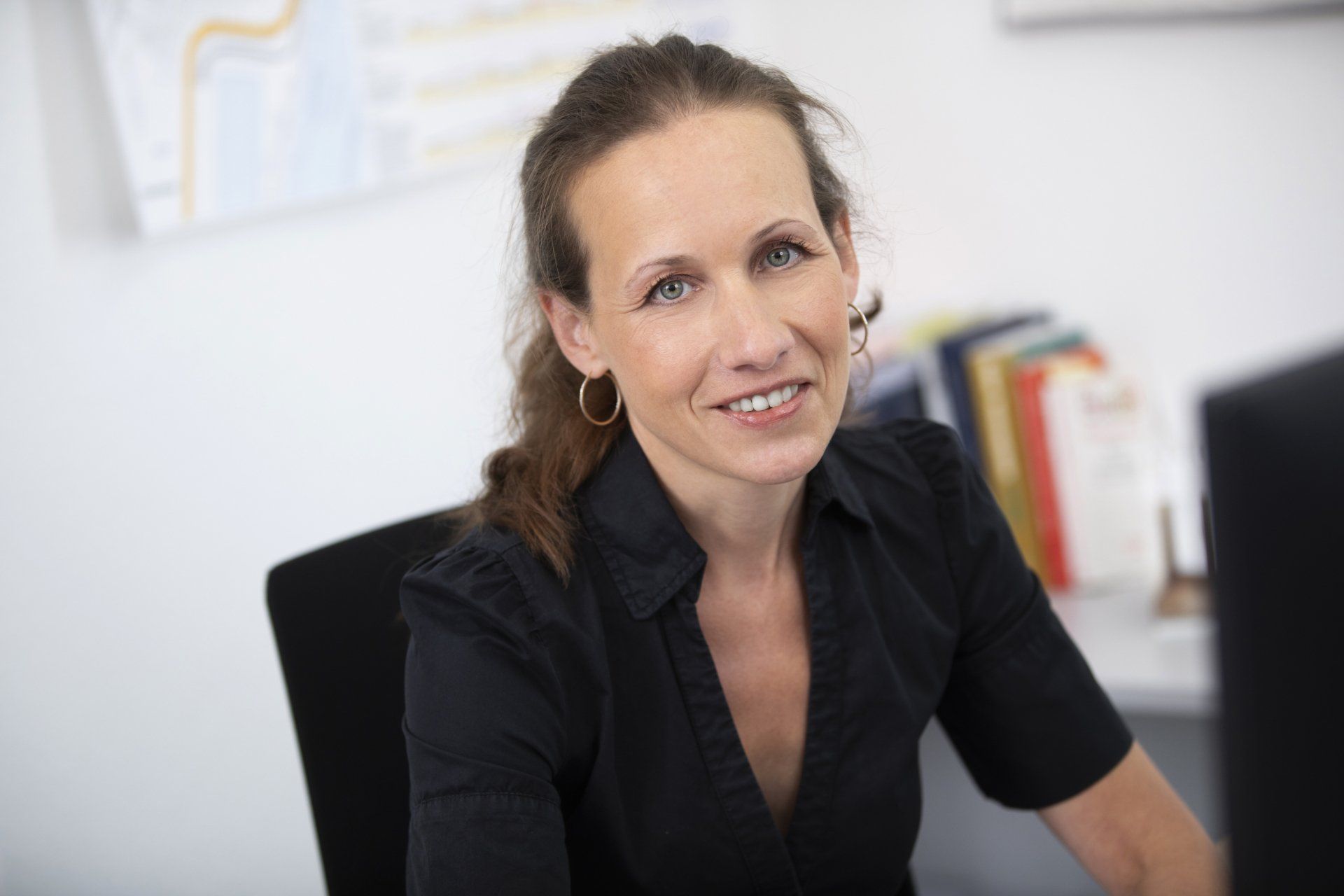 Eine Frau sitzt an einem Schreibtisch vor einem Computer und lächelt.