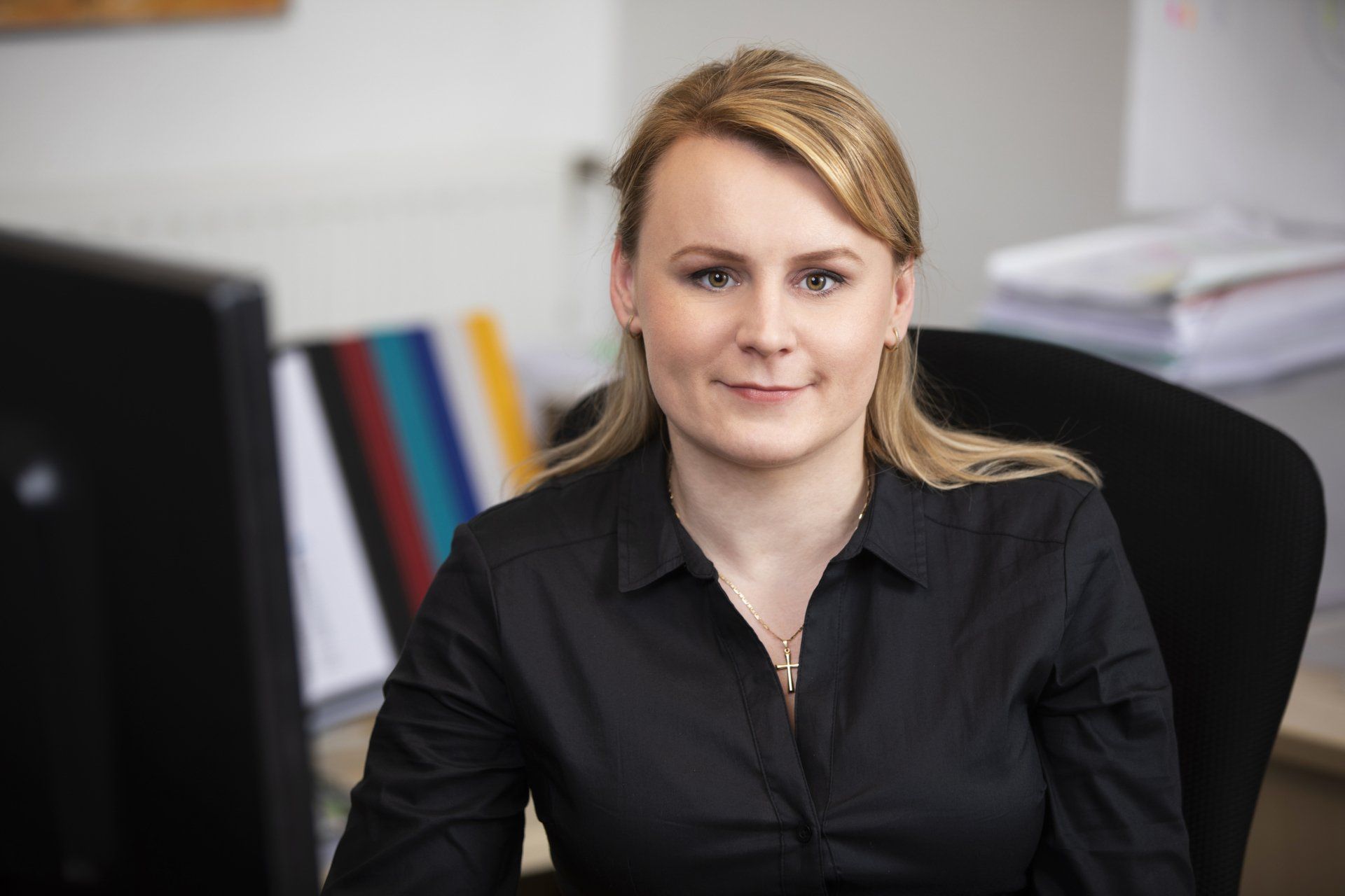 Eine Frau in einem schwarzen Hemd sitzt an einem Schreibtisch vor einem Computermonitor.