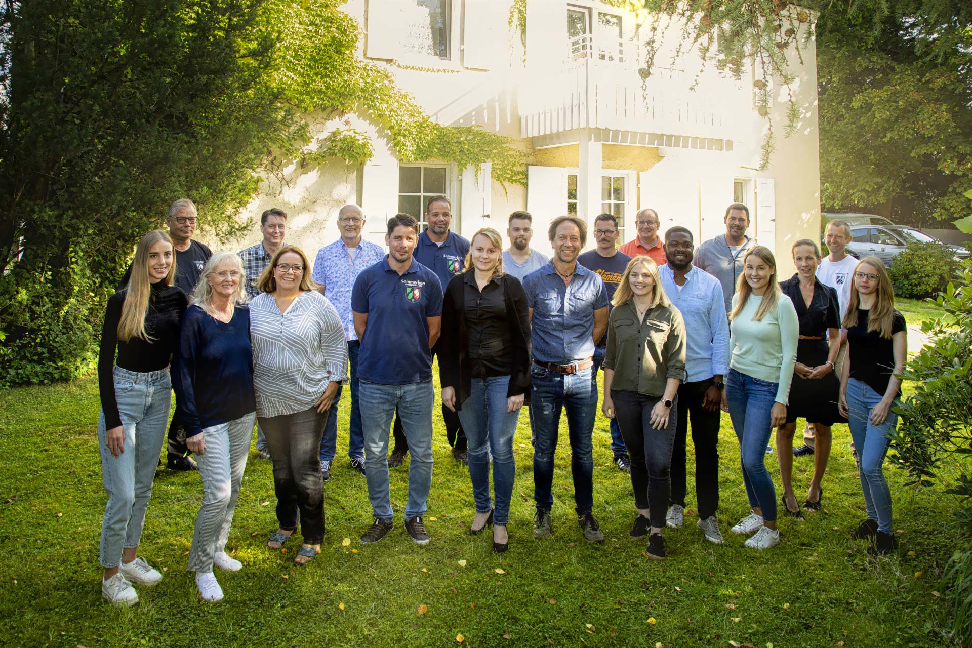 Eine Gruppe von Menschen posiert vor einem Haus für ein Foto.