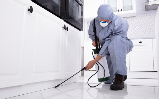 Technician in blue coveralls cleaning a white kitchen floor with a steam cleaner