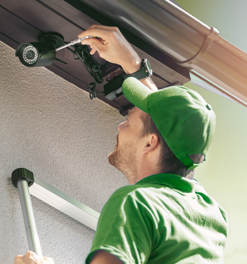 Worker in green uniform adjusting a ladder near a gutter on a house exterior
